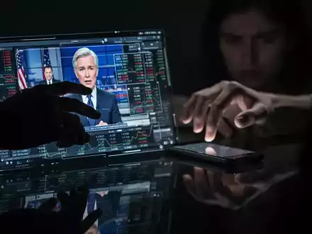 Eine Hand manipuliert ein Deepfake-Video eines Nachrichtensprechers auf einem Bildschirm, während im Hintergrund eine andere Hand ein Smartphone ergreift. - Foto: über boerse-global.de