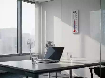 Ein modernes Büro mit einem Schreibtisch, Laptop, Wasserglas und einem Thermometer, das 28°C anzeigt, bei hellem Tageslicht. - Foto: über boerse-global.de