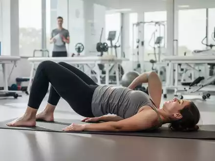 Eine Person führt eine Rückenübung auf einer Yogamatte in einem modernen, hellen Raum aus, fokussiert auf Bewegungstherapie. - Foto: über boerse-global.de