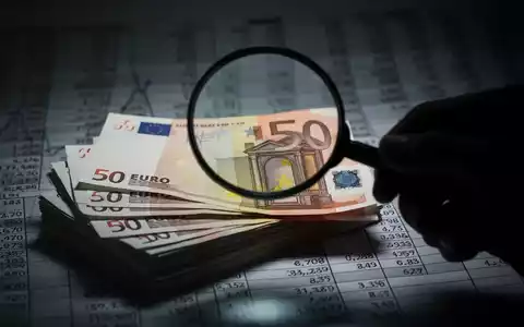 Ein Nahaufnahme von Euro-Banknoten, teilweise verdeckt von einer Hand mit einer Lupe, die finanzielle Prüfung und Untersuchung symbolisiert. - Foto: über boerse-global.de