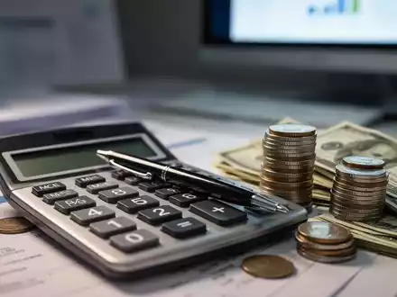 Ein Taschenrechner mit Stift, umgeben von Münzen und Geldscheinen, symbolisiert Finanzplanung und neue Kleinunternehmerregelungen. - Foto: über boerse-global.de