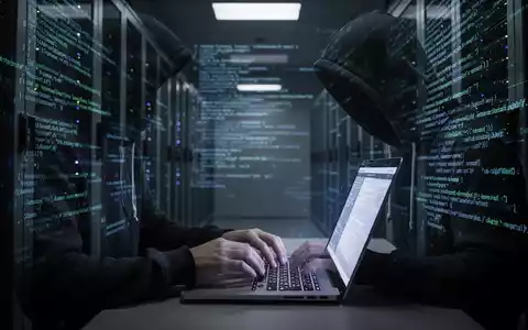 Eine Person im Kapuzenpullover tippt an einem Laptop in einem dunklen Serverraum, mit digitalem Code an den Wänden. Fokus auf Hände und Bildschirm. - Foto: über boerse-global.de