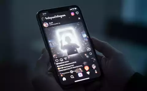 Nahaufnahme eines iPhone-Bildschirms mit Instagram Reels und hellem, überbelichtetem Glühen, gehalten in einer Hand in einem schwach beleuchteten Raum. - Foto: über boerse-global.de