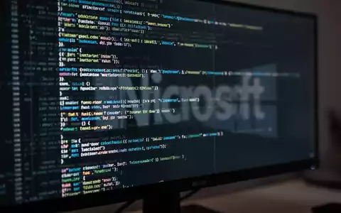 Stilisierte Nahaufnahme eines Computermonitors mit abstraktem Code und CLI-Elementen, dezente Microsoft-Logo-Reflexion. - Foto: über boerse-global.de