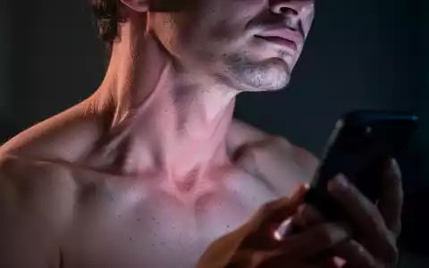 Nahaufnahme einer Person mit sichtbaren Nacken- und Schulterverspannungen, beleuchtet vom Schein eines Smartphones. - Foto: über boerse-global.de