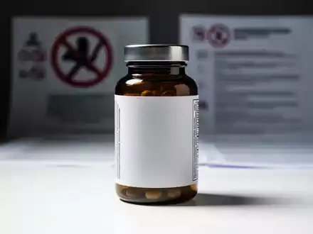 Eine generische Flasche Nahrungsergänzungsmittel auf einer weißen Oberfläche, unscharf im Hintergrund sind Symbole des Verbraucherschutzes. - Foto: über boerse-global.de