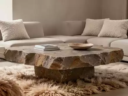 Ein minimalistisches Wohnzimmer mit einem groben Naturstein-Couchtisch, weichen Bouclé-Kissen und einem Flokati-Teppich. - Foto: über boerse-global.de