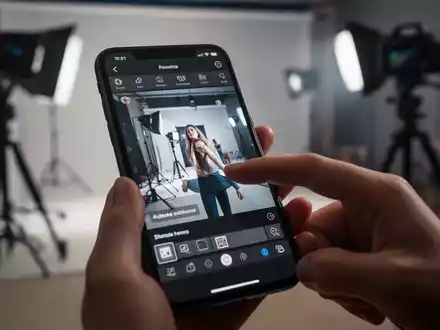 Nahaufnahme einer Hand, die mit einem Smartphone ein Foto in einer App bearbeitet, professionelles Fotostudio im Hintergrund. - Foto: über boerse-global.de