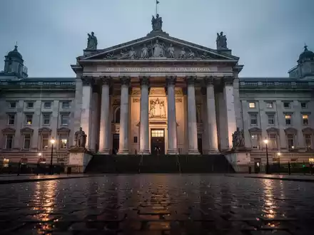 Ein dramatisches, schräges Foto eines imposanten Gerichtsgebäudes mit nassen Kopfsteinpflastern, die die Stadtlichter reflektieren. - Foto: über boerse-global.de