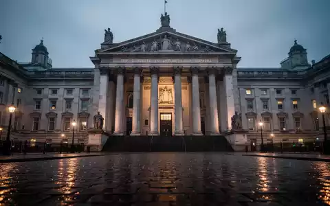 Ein dramatisches, schräges Foto eines imposanten Gerichtsgebäudes mit nassen Kopfsteinpflastern, die die Stadtlichter reflektieren. - Foto: über boerse-global.de