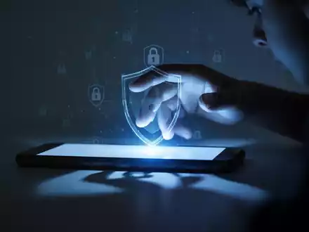 Ein Smartphone-Bildschirm mit leuchtendem blauem Licht, das auf eine unscharfe Hand fällt, mit digitalen Schloss-Symbolen. - Foto: über boerse-global.de