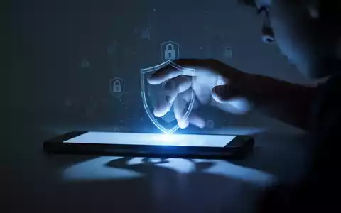 Ein Smartphone-Bildschirm mit leuchtendem blauem Licht, das auf eine unscharfe Hand fällt, mit digitalen Schloss-Symbolen. - Foto: über boerse-global.de