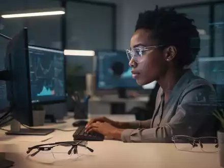 Eine Person mit Brille arbeitet konzentriert an einem Computer in einem modernen Büro. Eine spezielle Bildschirmarbeitsplatzbrille liegt daneben. - Foto: über boerse-global.de