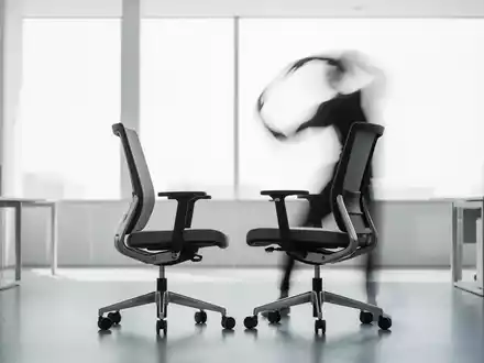 Eine Person macht Dehnübungen neben einem ergonomischen Bürostuhl in einem modernen, hellen Büro. - Foto: über boerse-global.de