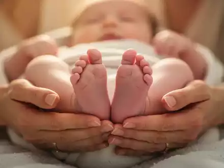 Nahaufnahme der Hände einer Mutter, die sanft die Füße ihres Babys halten, in warmem, beruhigendem Licht. - Foto: über boerse-global.de