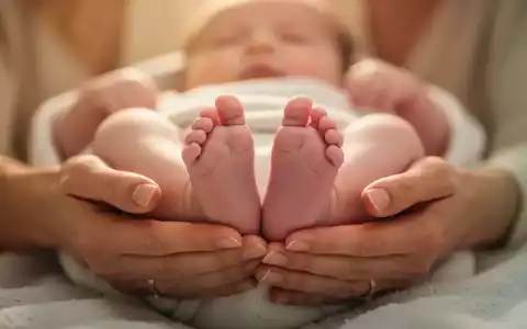 Nahaufnahme der Hände einer Mutter, die sanft die Füße ihres Babys halten, in warmem, beruhigendem Licht. - Foto: über boerse-global.de