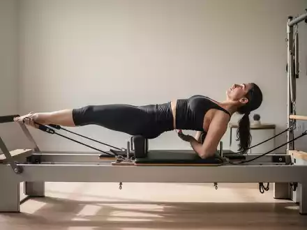Eine Person führt eine Pilates-Übung auf einem modernen Reformer-Gerät in einem minimalistischen Studio aus. - Foto: über boerse-global.de
