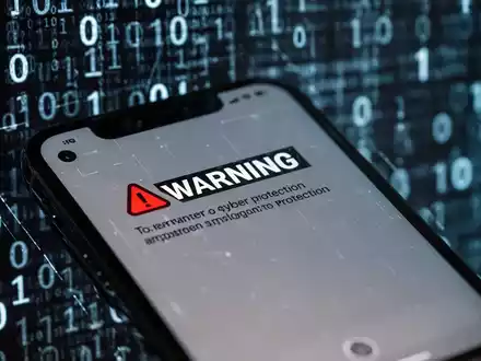 Nahaufnahme eines iPhone-Bildschirms mit einer 'Bösartige Nachricht erkannt'-Warnung, unscharfer digitaler Code im Hintergrund. - Foto: über boerse-global.de