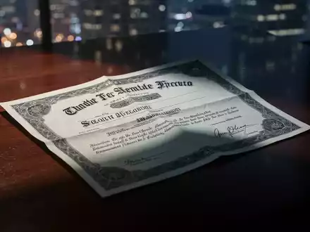 Ein zerknittertes Wertpapier auf einem dunklen Holztisch, teilweise im Schatten, mit verschwommenen Stadtlichtern im Hintergrund. - Foto: über boerse-global.de