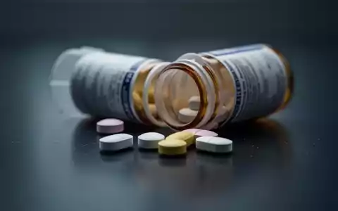 Eine Nahaufnahme zeigt eine unscharfe Pillendose und lose Tabletten auf einer dunklen, spiegelnden Oberfläche. - Foto: über boerse-global.de