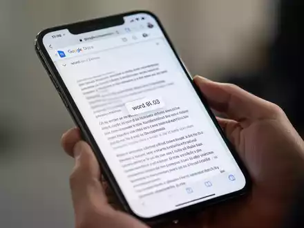 Ein Smartphone-Bildschirm zeigt ein Google Docs-Dokument mit sichtbarer Wortanzahl, gehalten in einer Hand. - Foto: über boerse-global.de