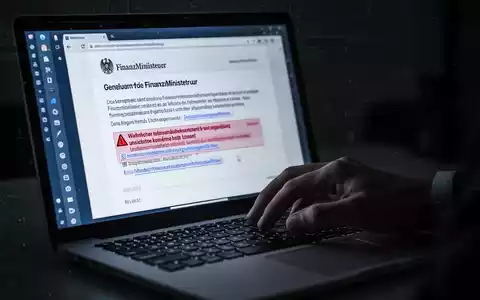 Eine Hand tippt auf einem Laptop, auf dessen Bildschirm eine gefälschte E-Mail des Finanzministeriums mit schädlichen Links zu sehen ist. - Foto: über boerse-global.de