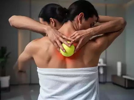 Eine Person massiert ihren Rücken mit einem in ein Handtuch gewickelten Tennisball, um Faszien zu lockern und Verspannungen zu lösen. - Foto: über boerse-global.de