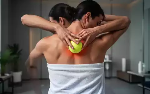 Eine Person massiert ihren Rücken mit einem in ein Handtuch gewickelten Tennisball, um Faszien zu lockern und Verspannungen zu lösen. - Foto: über boerse-global.de