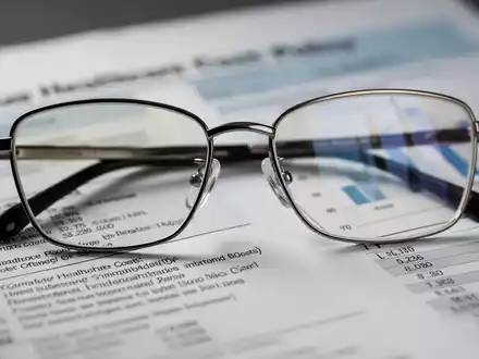 Eine stilvolle Brille liegt auf einem unscharfen Finanzdokument, das Gesundheitskosten und Politik symbolisiert. - Foto: über boerse-global.de