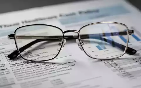 Eine stilvolle Brille liegt auf einem unscharfen Finanzdokument, das Gesundheitskosten und Politik symbolisiert. - Foto: über boerse-global.de