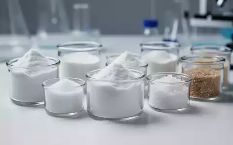 Nahaufnahme verschiedener Süßstoffe und Zuckeralternativen in kleinen Behältern auf einer weißen Oberfläche, die eine Laborumgebung andeutet. - Foto: über boerse-global.de