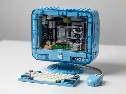 Detailliertes LEGO-Modell des Bondi Blue Apple iMac G3 mit durchsichtigen blauen Steinen, die innere Komponenten zeigen, neben einer Miniatur-LEGO-Tastatur und -Maus. - Foto: über boerse-global.de