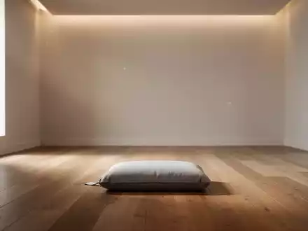 Ein ruhiger, minimalistischer Raum mit einem einzelnen Meditationskissen auf einem Holzboden, weiches, indirektes Licht fällt herein. - Foto: über boerse-global.de