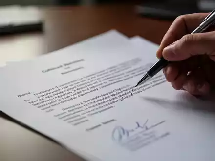Nahaufnahme eines rechtlichen Dokuments, das von einer Hand mit einem Stift gehalten wird, mit einem unscharfen Bürohintergrund. - Foto: über boerse-global.de