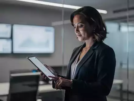 Barbara Venneman prüft Aktienkurse auf einem Tablet in einem modernen Büro, das Finanzdaten anzeigt. - Foto: über boerse-global.de