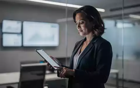 Barbara Venneman prüft Aktienkurse auf einem Tablet in einem modernen Büro, das Finanzdaten anzeigt. - Foto: über boerse-global.de