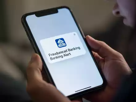 Nahaufnahme eines Smartphone-Bildschirms mit betrĂŒgerischer Bankwarnung, in den HĂ€nden einer Person. - Foto: ĂŒber boerse-global.de