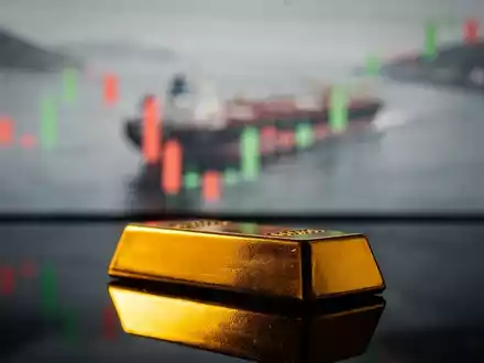 Ein goldener Barren mit verschwommenem Hintergrund, der eine Ölroute und einen Finanzchart zeigt. - Foto: über boerse-global.de