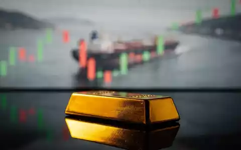 Ein goldener Barren mit verschwommenem Hintergrund, der eine Ölroute und einen Finanzchart zeigt. - Foto: über boerse-global.de