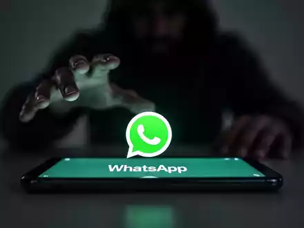 Ein Smartphone mit WhatsApp-Logo, im Hintergrund eine verschwommene Schattenfigur, die danach greift. - Foto: über boerse-global.de