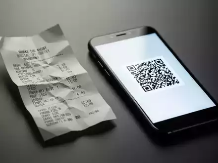 Eine zerknüllte Papierrechnung liegt neben einem Smartphone, das einen QR-Code anzeigt, der den Übergang zu digitalen Belegen symbolisiert. - Foto: über boerse-global.de