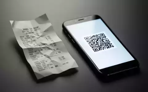 Eine zerknüllte Papierrechnung liegt neben einem Smartphone, das einen QR-Code anzeigt, der den Übergang zu digitalen Belegen symbolisiert. - Foto: über boerse-global.de