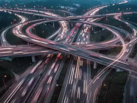 Eine komplexe Autobahnkreuzung bei Dämmerung mit Lichtspuren von Autos, die die Herausforderungen im Arbeits- und Verkehrsrecht symbolisieren. - Foto: über boerse-global.de