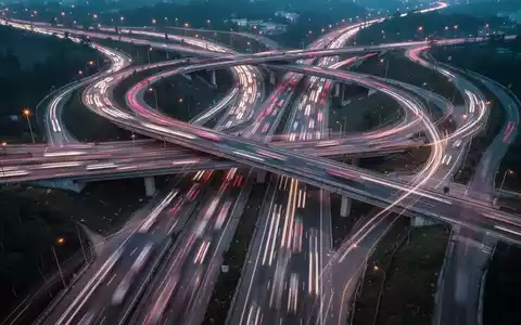 Eine komplexe Autobahnkreuzung bei Dämmerung mit Lichtspuren von Autos, die die Herausforderungen im Arbeits- und Verkehrsrecht symbolisieren. - Foto: über boerse-global.de