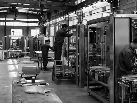 Schwarzweiß-Reportagefoto zur Krones AG DE0006335003 dokumentiert Arbeiter beim Zusammenbau industrieller Verpackungsmaschinen in großer Fertigungshalle authentisch - Foto: THN