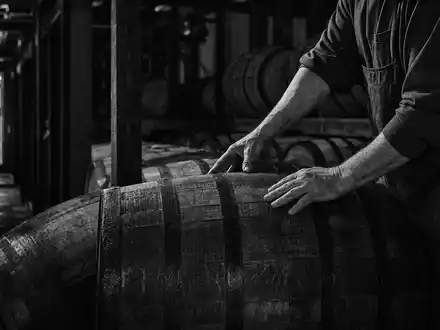 Brown-Forman Corp. US1170431092 dokumentarisch: Handwerker rollt schweres Bourbon-Eichenfass im Kentucky-Rickhouse in Schwarzweiß-Reportage - Foto: THN