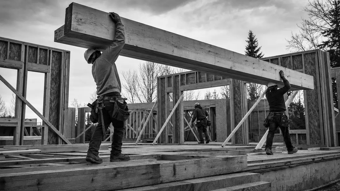 Schwarzweiß-Reportage: Zimmerleute heben Holzbalken beim Hausbau