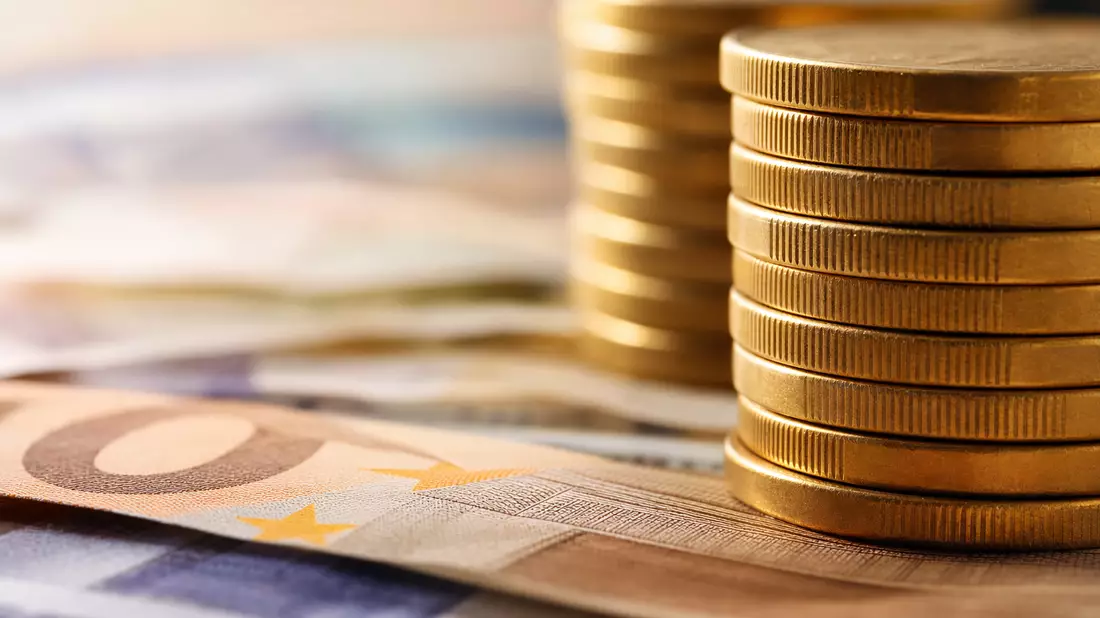 Extreme Nahaufnahme gestapelter Goldmünzen vor unscharfen Euro-Banknoten im Hintergrund