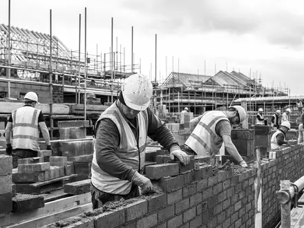 Bellway p.l.c. (GB0000904986) zeigt Handwerker beim Mauern, eine dokumentarische Schwarzweiß-Aufnahme einer britischen Baustelle heute - Foto: THN