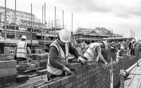 Bellway p.l.c. (GB0000904986) zeigt Handwerker beim Mauern, eine dokumentarische Schwarzweiß-Aufnahme einer britischen Baustelle heute - Foto: THN
